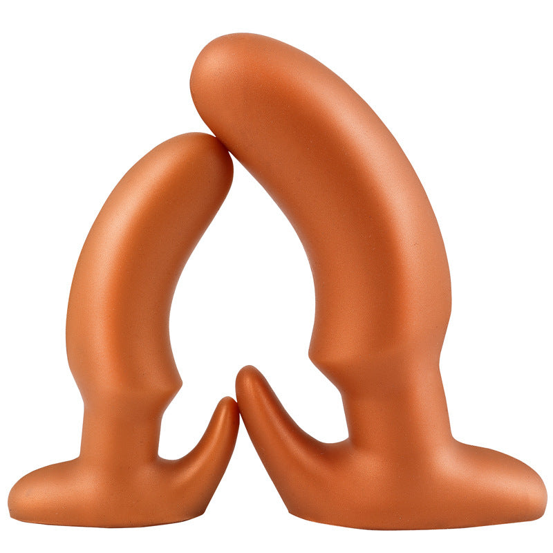 Two gold tapered silicone butt plugs arched against each other showing the curved shaft profile