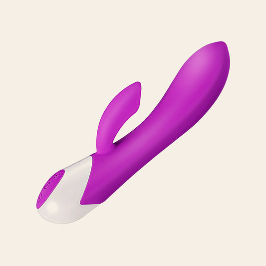 Purple silicone rabbit vibrator with a curved shaft, clitoral arm and white base, on a soft beige background — Femme Bliss BlissButterfly
