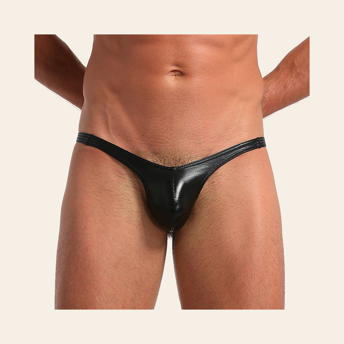 Model wearing the men's metallic thong in glossy black with a contoured pouch, on a soft beige background