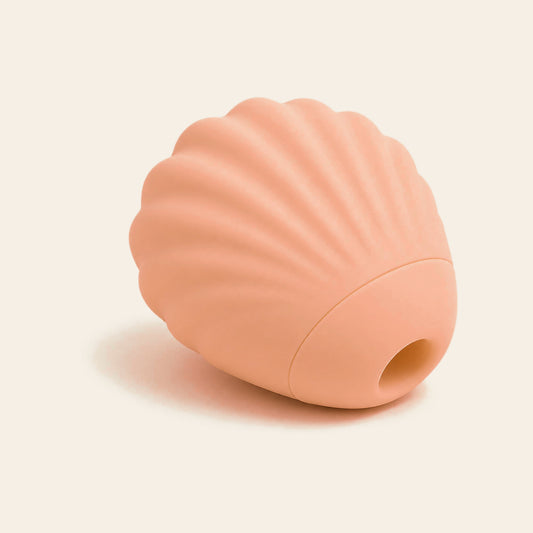 Peach-pink shell-shaped suction vibrator with a round suction opening, on a soft beige background — Femme Bliss SeaShell Bliss